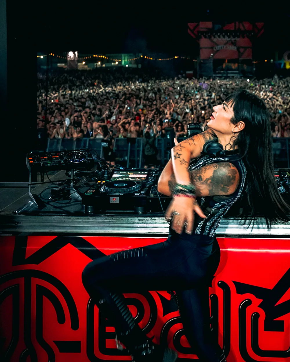 Fatima seated beside the decks, looking up, with the crowd behind her